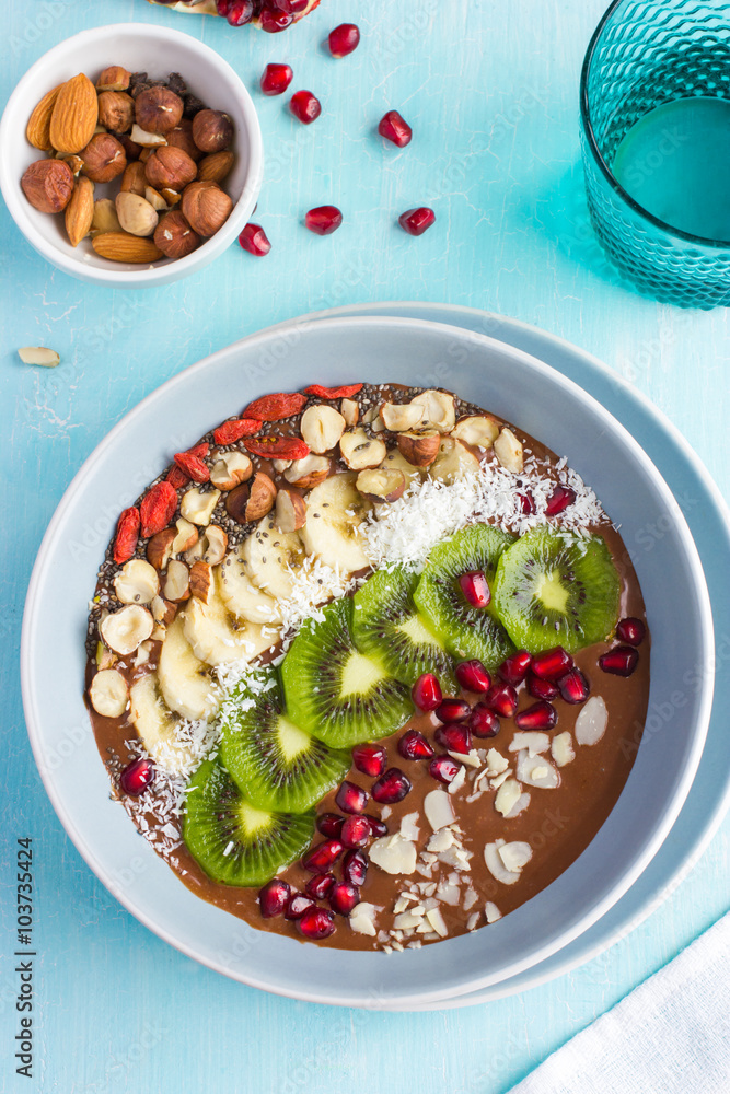 bowl of chocolate smoothie  with fruits nuts on blue background
