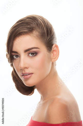 Young adorable brunette woman with cute makeup low bun hairstyle in red shirt with bare shoulders looking into camera with curiosity posing on white studio background