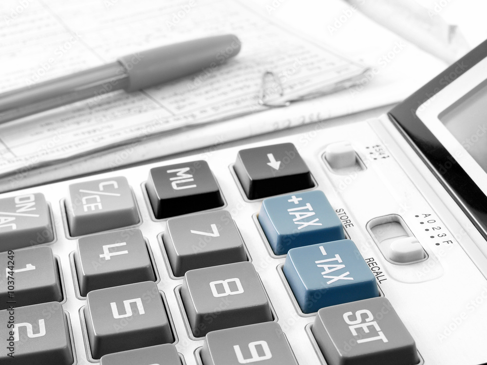 blue tax buttons on white calculator and pen on pile of financial documents blue tax buttons on white calculator and pen on pile of financial documents