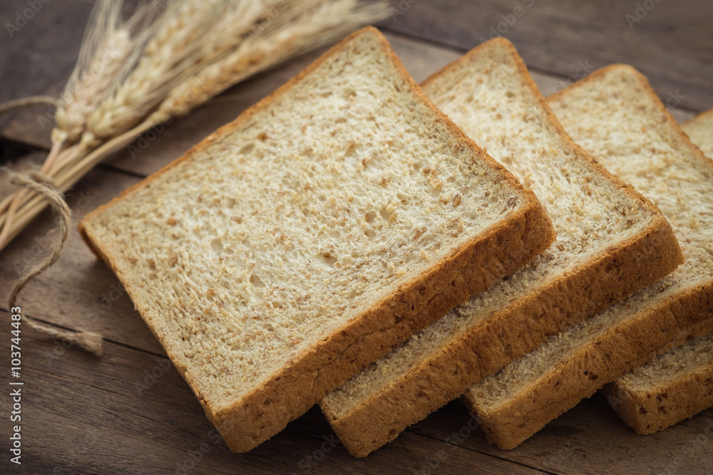 Whole wheat bread slices and wheat on wooden table Whole wheat bread slices and wheat on wooden table