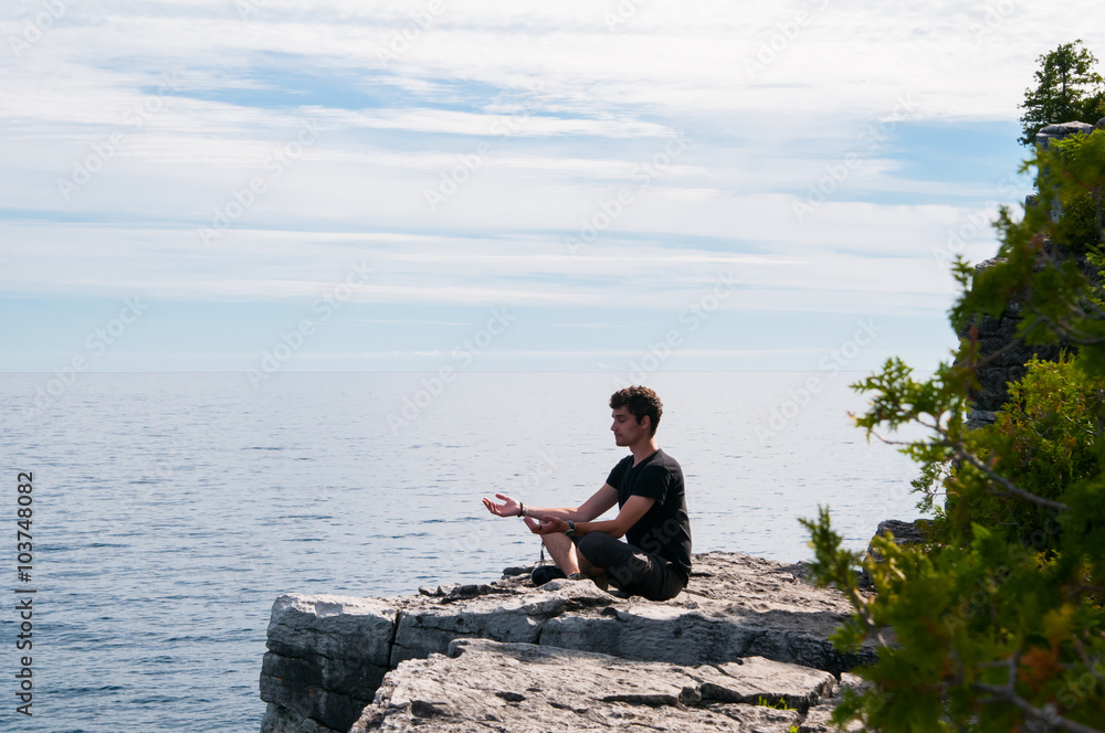 teenage boy sitting on a rock overlooking a lake meditating