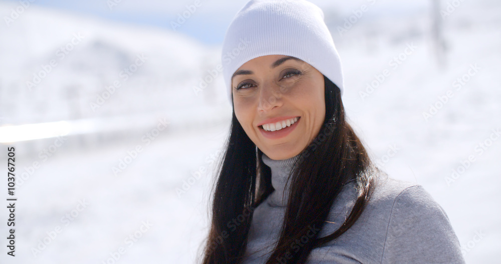 Fototapeta premium Gorgeous young woman in winter fashion in a snowy landscape looking at the camera with a lovely warm friendly smile with copy space