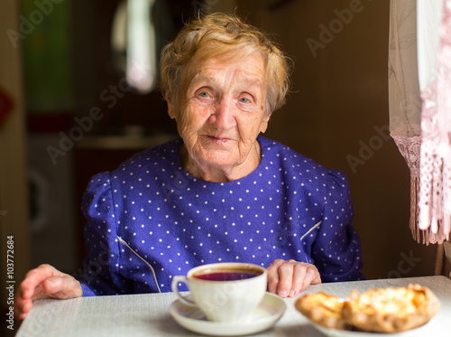 An elderly woman sitting in the kitchen drinking tea.
