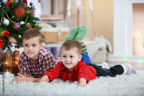 Two cute small brothers lie on carpet on Christmas tree background