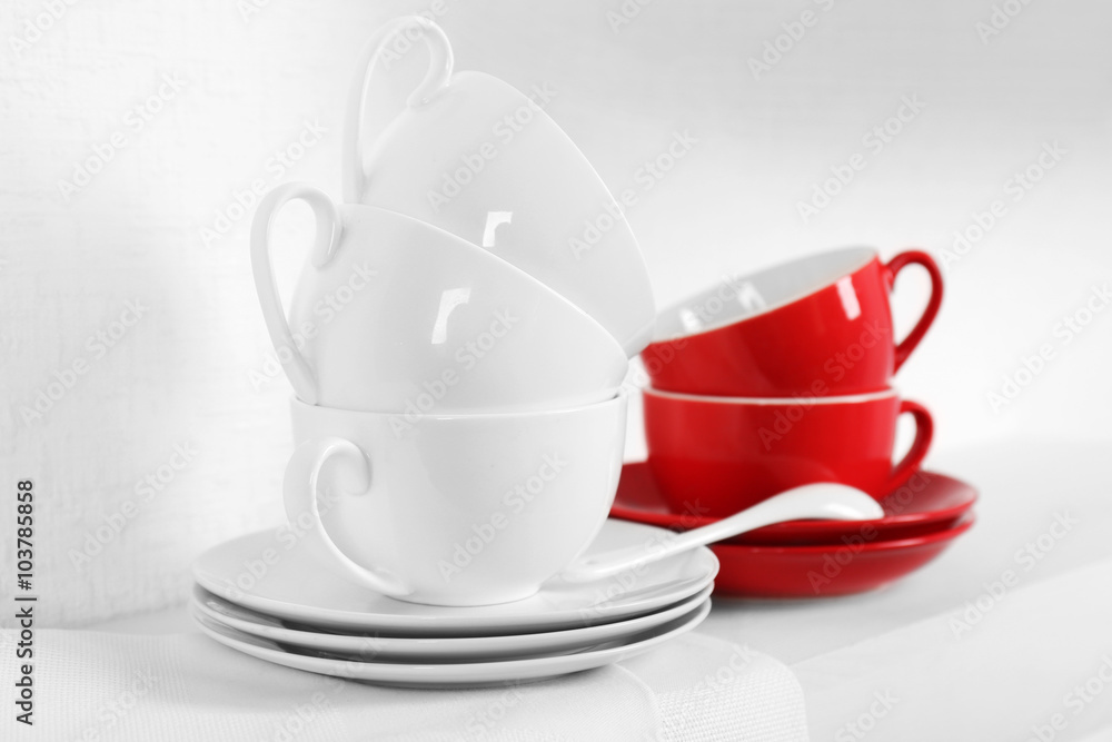 Set of cups and saucers with napkin on shelf against white wall background Set of cups and saucers with napkin on shelf against white wall background