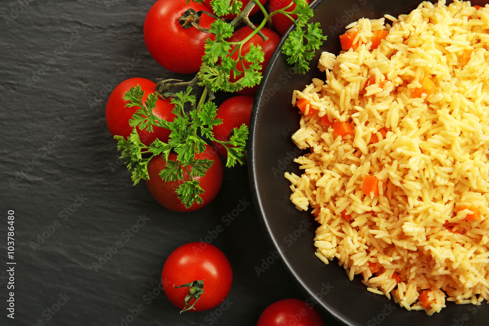 Stewed rice with a carrot and tomatoes on a plate over black background, close up Stewed rice with a carrot and tomatoes on a plate over black background, close up