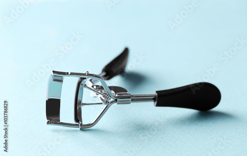 Eyelash curler with black handles on a blue background, close up