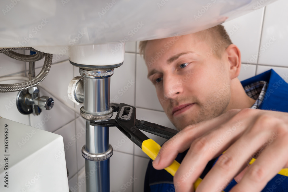 Young Male Plumber Fixing Sink In Kitchen Young Male Plumber Fixing Sink In Kitchen