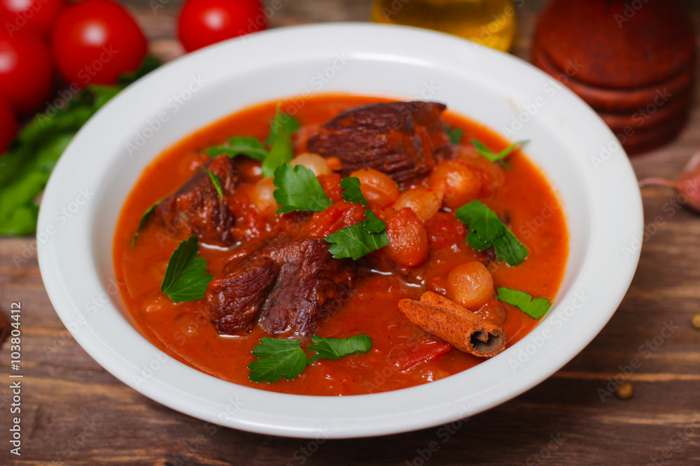National Greek dish stifado with beef, tomatoes and onions, stewed in red wine with Herbs on a wooden background, horizontal National Greek dish stifado with beef, tomatoes and onions, stewed in red wine with Herbs on a wooden background, horizontal