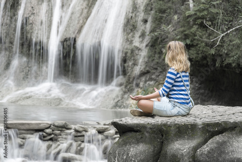 Young girl meditating at the waterfall