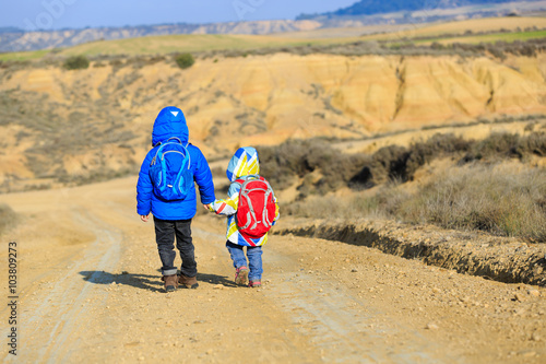 little boy and girl with backpacks travel on the road to mountains
