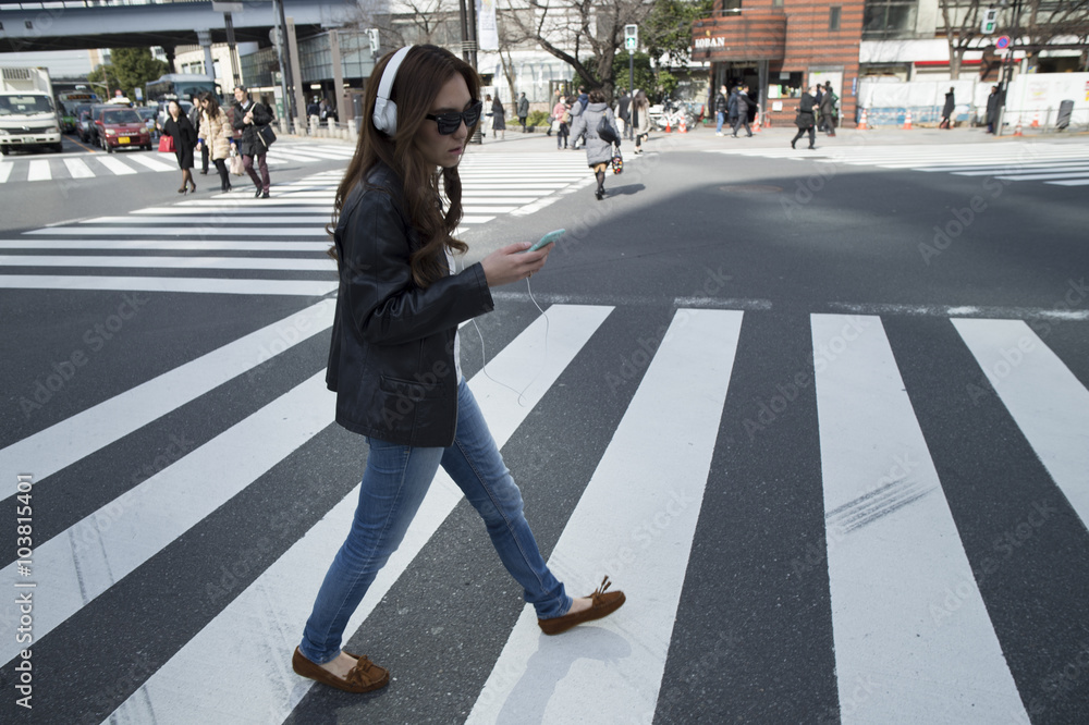 Fototapeta premium Young woman is walking the crosswalk with a headphone