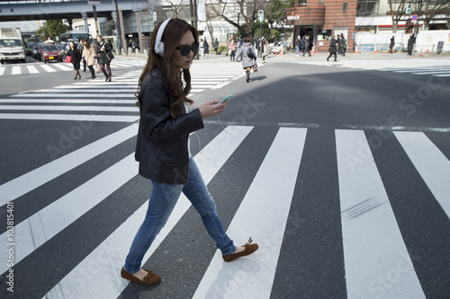 Young woman is walking the crosswalk with a headphone