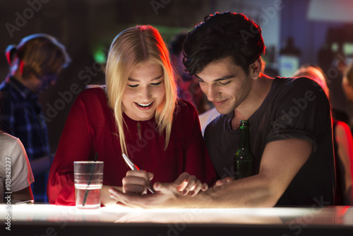 Young man is flirting with attractive woman at bar writing number on his hand photo