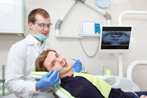 Young Man in dentost chair having teeth examined at dentists. Young Male dentist. X-ray on background