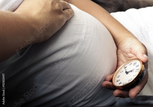 Pregnant belly and ticking cloc in mom's hand  photo