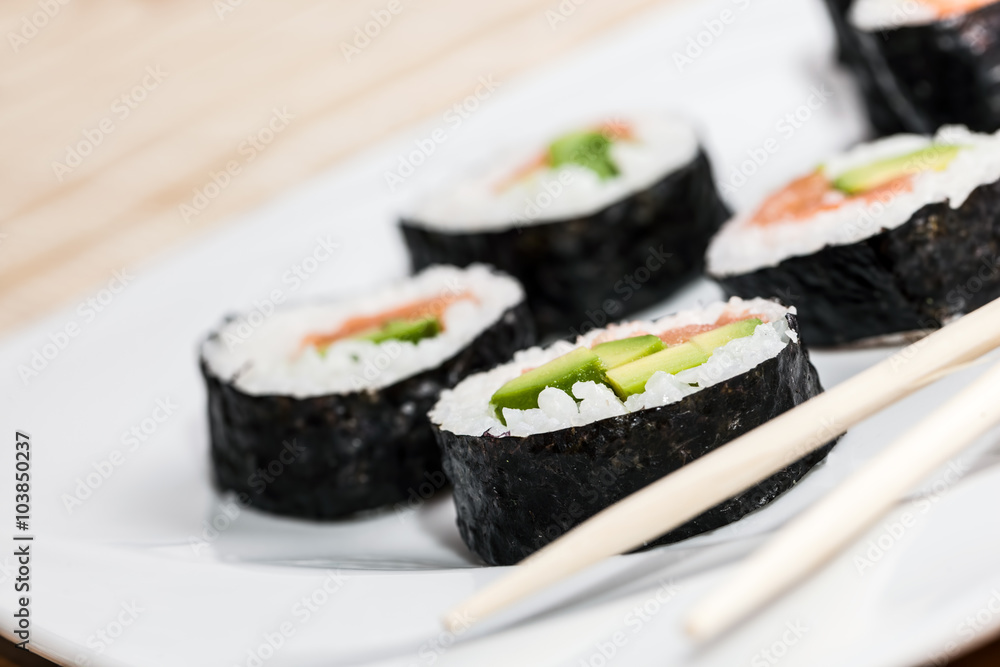 Sushi with salmon, avocado, rice in seaweed and chopsticks on a plate. Sushi with salmon, avocado, rice in seaweed and chopsticks on a plate.