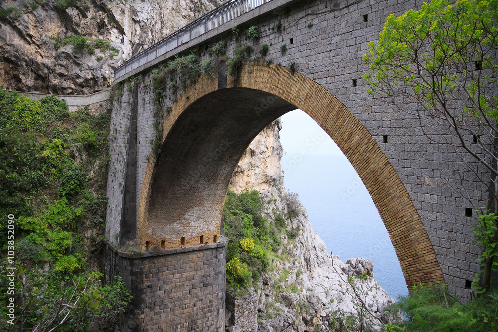 Arched bridge between rocks and sea and sky visible beneath it 