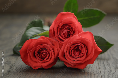 three red roses on wooden table  shallow focus
