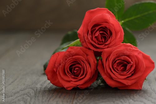 three red roses on wooden table, shallow focus