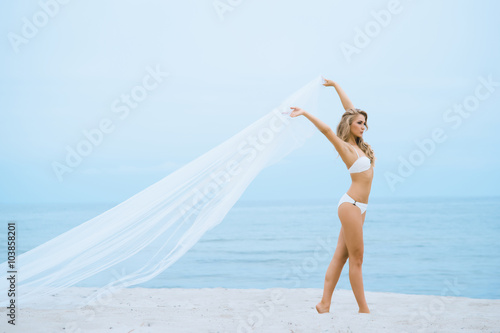 Gorgeous woman with hot legs posing with a blowing silk on the beach.