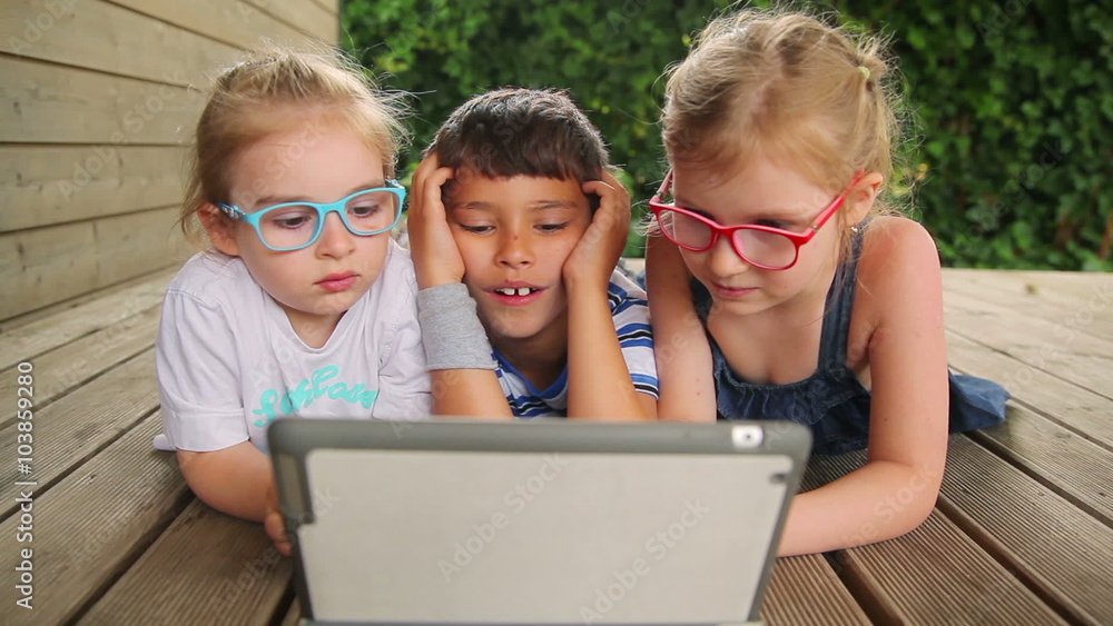 Children play on the tablet while lying on the wooden floor Children play on the tablet while lying on the wooden floor