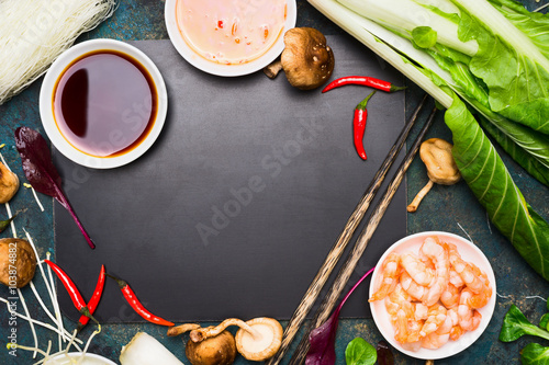 Chinese or Thai cooking food background. Asian food ingredients : soy sauce, chopsticks, rice noodles , pok choi,  shiitake mushrooms and scampi on black blank chalkboard, top view.
