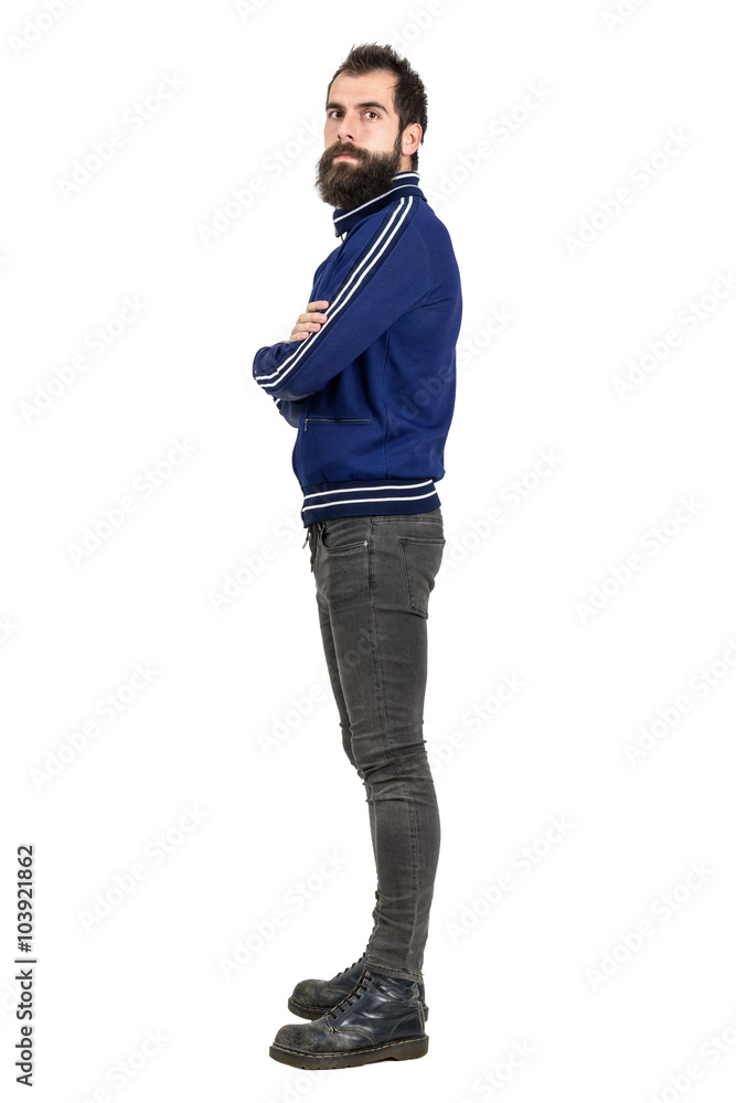 Side view of bearded punker in tracksuit jacket serious looking at camera. Full body length portrait isolated over white studio background. Side view of bearded punker in tracksuit jacket serious looking at camera. Full body length portrait isolated over white studio background.