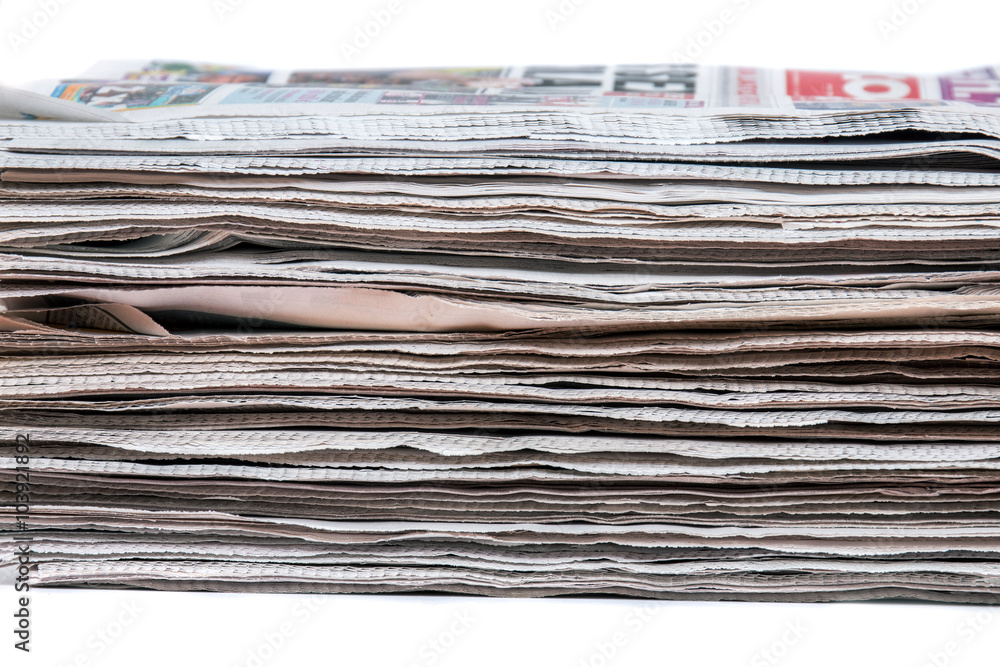 View of a pile of newspapers stacked isolated on a white background. View of a pile of newspapers stacked isolated on a white background.