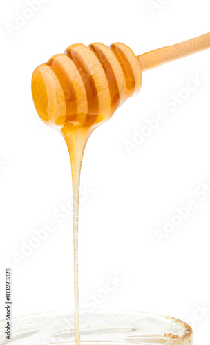 honey flows down from wooden stick to glass jar