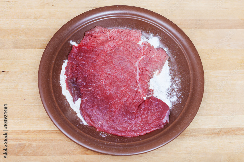 raw veal schnitzel breaded in flour on plate raw veal schnitzel breaded in flour on plate