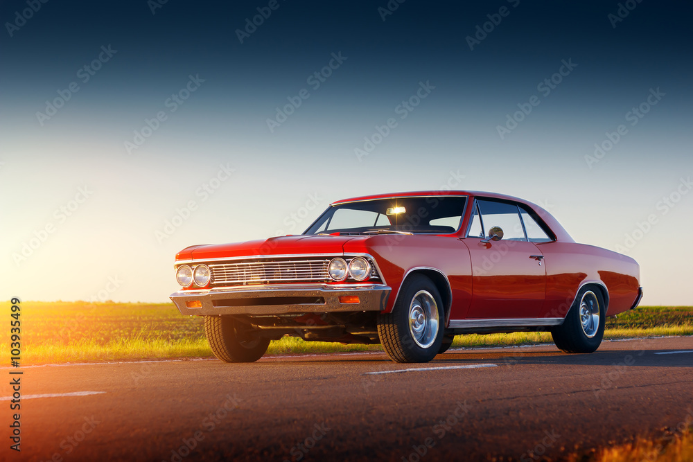 Obraz premium Samochód retro czerwony pobyt na drodze asfaltowej o zachodzie słońca