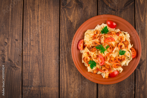 Fettuccine pasta with shrimp tomatoes and herbs. wooden background
