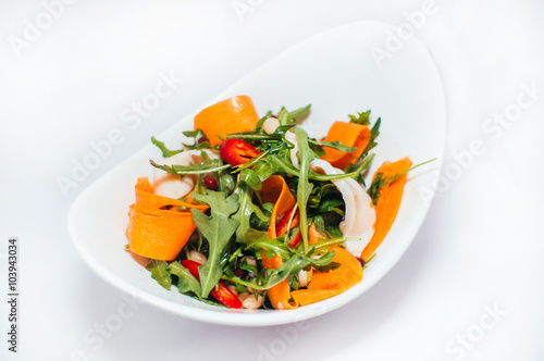 Fresh vegetarian salad with arugula and carrots on a white plate isolated