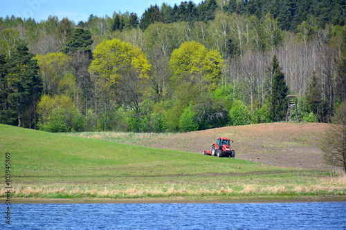 Sunny and green landscape with lake and tractor