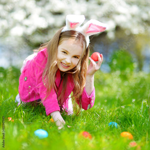 Adorable little girl hunting for easter egg in blooming spring garden