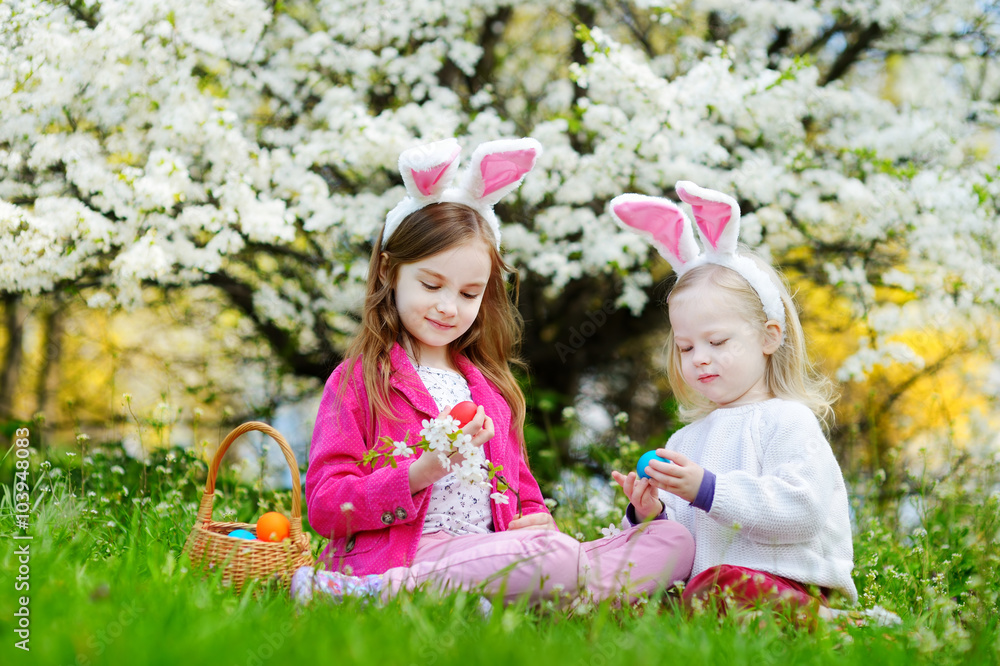 Two adorable little sisters hunting for easter egg in blooming spring garden Two adorable little sisters hunting for easter egg in blooming spring garden