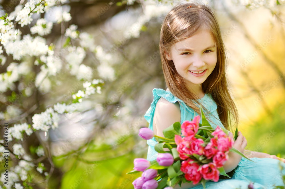 Adorable little girl holding tulips for her mother in blooming cherry garden Adorable little girl holding tulips for her mother in blooming cherry garden