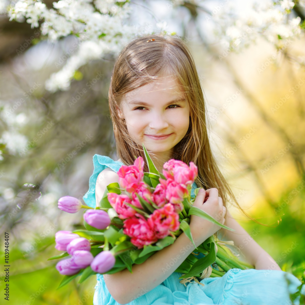 Adorable little girl holding tulips for her mother in blooming cherry garden Adorable little girl holding tulips for her mother in blooming cherry garden