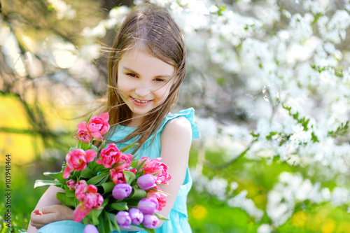 Adorable little girl holding tulips for her mother in blooming cherry garden
