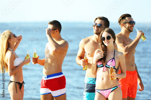 Happy young friends drinking beer at the beach, outdoors © Africa Studio