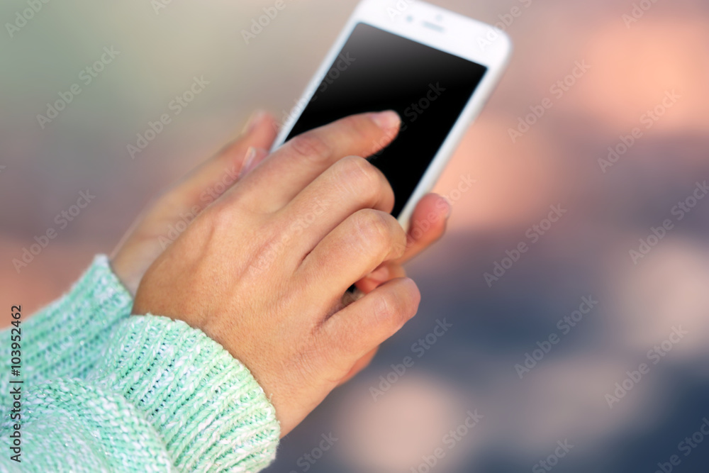 Female hands holding a mobile phone outdoors, on blurred background