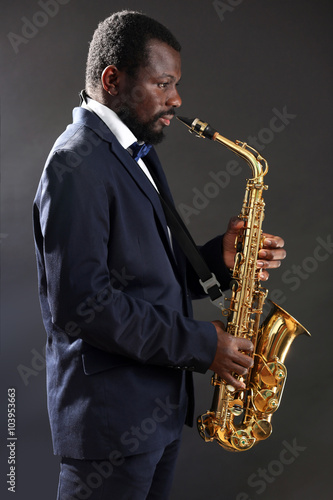 African American jazz musician playing the saxophone on grey background