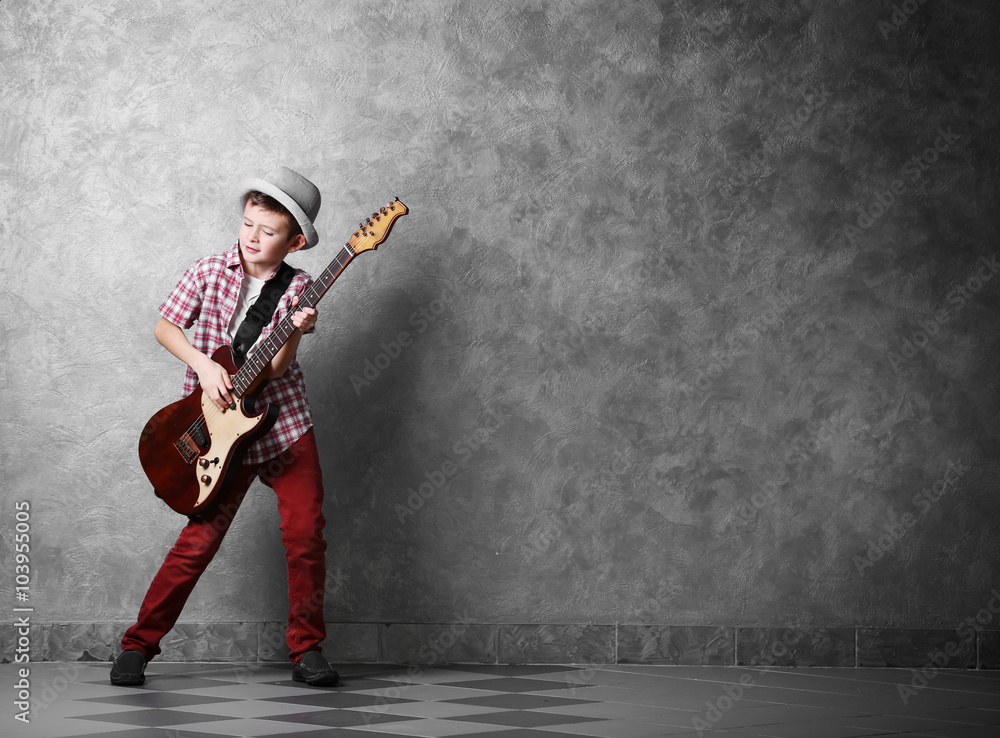 Little boy playing guitar on a grey wall background Little boy playing guitar on a grey wall background