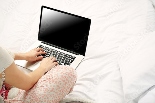 Woman in pajamas using laptop on her bed