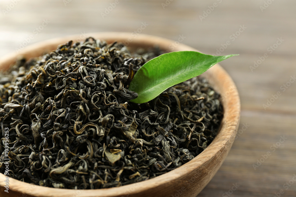 Dry tea with green leaves in bowl on wooden table background Dry tea with green leaves in bowl on wooden table background