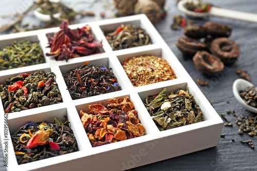 Variety of dry tea in wooden box with spoons on grey background