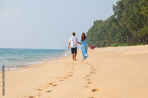 Honeymoon at the sea. Back view of loving couple walking away with footprints at sandy beach