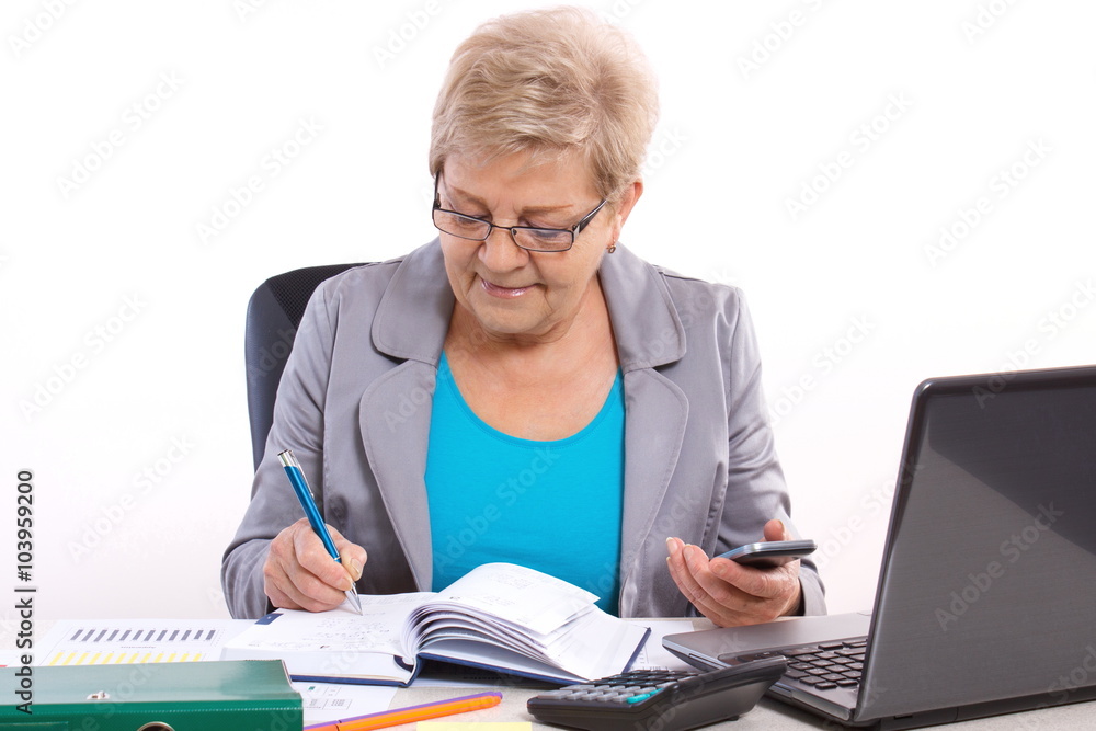 Elderly business woman writing in notebook and working at her desk in office, business concept Elderly business woman writing in notebook and working at her desk in office, business concept
