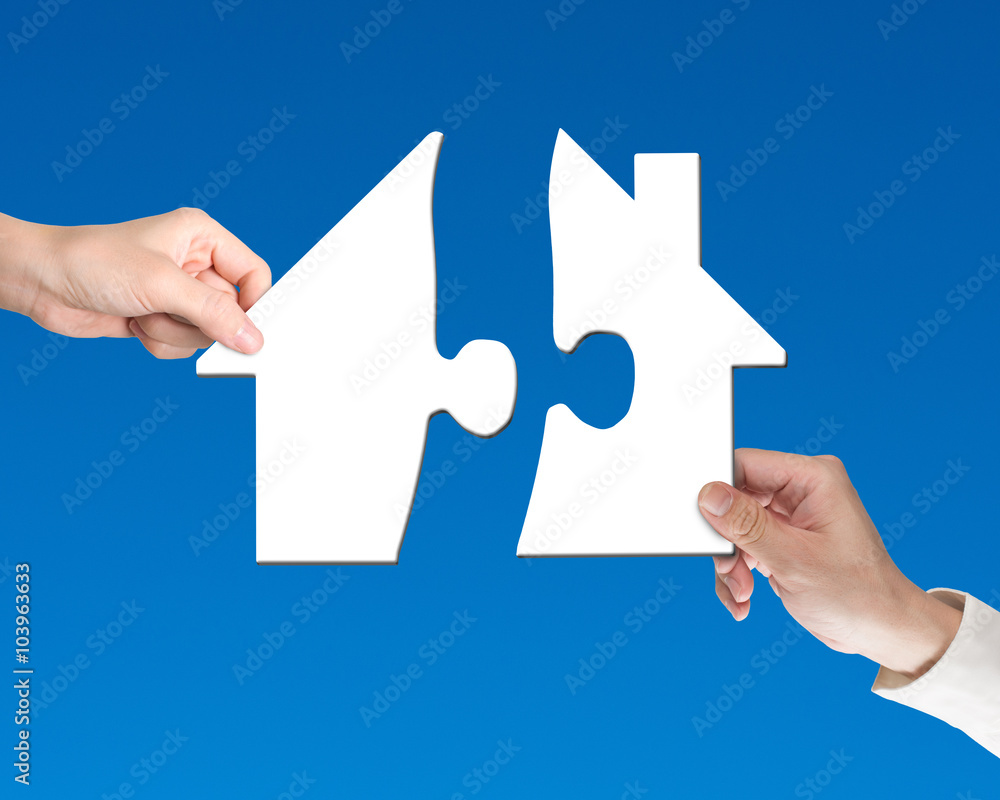 Two hands holding jigsaw pieces to finish house shape puzzle Two hands holding jigsaw pieces to finish house shape puzzle
